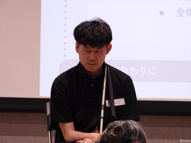 白杖を両手で持ち、静かに座っている真しろさん。黒髪の男性